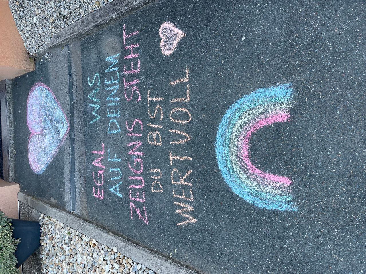 Eine Kreidetafel mit Kreideschrift in mehreren Farben, einschließlich eines Herzens, eines Regenbogens und der Phrase 'Egal was auf deinem Zeugnis steht bist du voll wertvoll'.