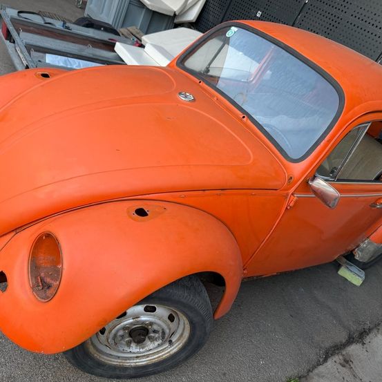 Ein alter orangefarbener Volkswagen Käfer steht auf der Straße. Das Auto hat einige Kratzer und Rost, sieht aber immer noch gut aus.