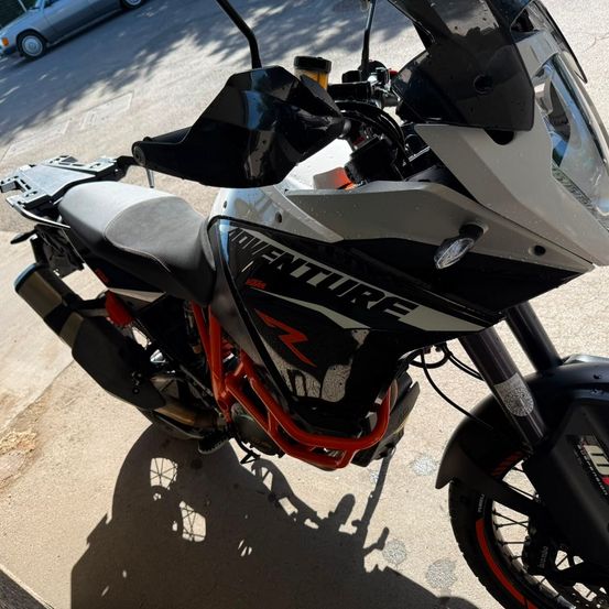 Ein schwarz-weißes KTM Adventure Motorrad ist am Straßenrand geparkt, mit einem Auto dahinter.