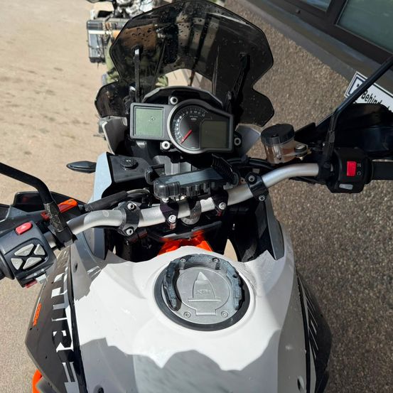 Eine Nahaufnahme des Armaturenbretts eines Motorrads mit Tachometer, Bildschirm und Lenker. Das Motorrad ist weiß und schwarz und auf einer asphaltierten Oberfläche geparkt.