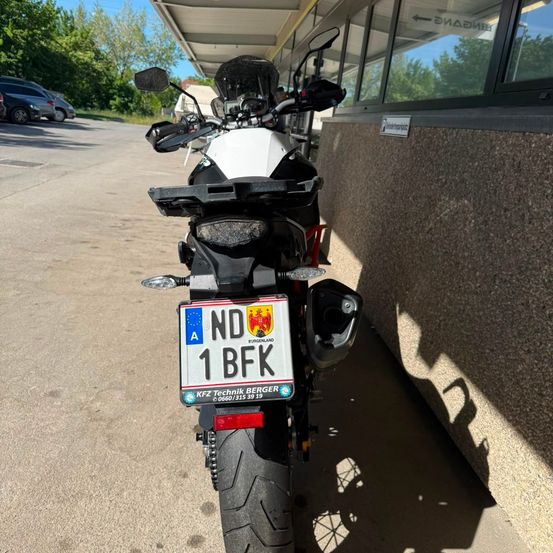 Ein Motorrad mit dem Kennzeichen ND 1 BFK ist neben einem Gebäude geparkt. Das Motorrad hat eine Windschutzscheibe und Spiegel.