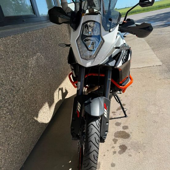 Ein KTM Adventure-Motorrad mit orangefarbenem Akzent ist an der Seite einer Straße in der Nähe eines Gebäudes geparkt.