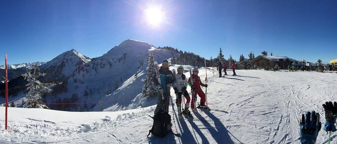 Drei Skifahrer posieren für ein Foto auf einem verschneiten Berg mit klarem blauem Himmel und Bergen im Hintergrund.
