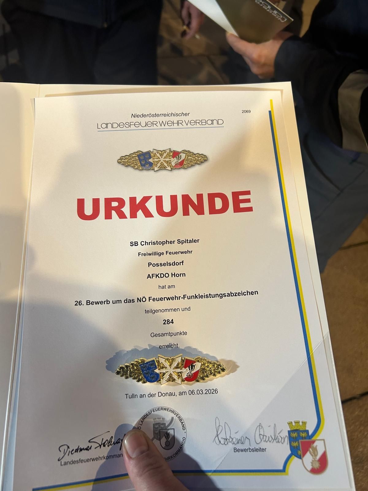 Ein Zertifikat der Österreichischen Vereinigung der Freiwilligen Feuerwehren. Es steht 'URKUNDE' in rot. Die Auszeichnung ist für das 26. NO Feuerwehr-Funktionsabzeichen, verliehen am 6. März 2026, in Tulln an der Donau.