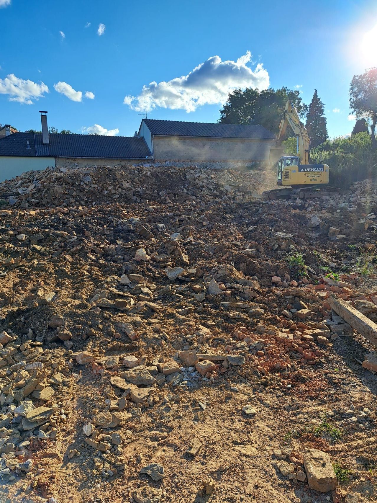 Ein gelber Bagger ist auf einer Baustelle und räumt Schutt und Trümmer unter einem klaren blauen Himmel.