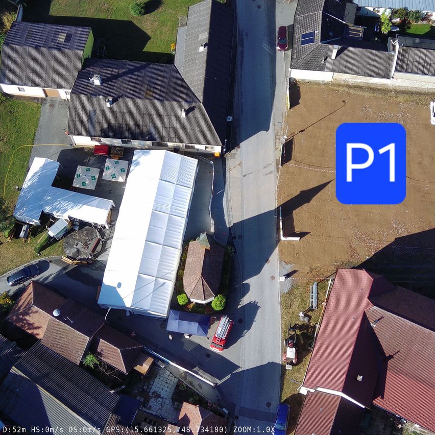 An aerial view of a small town with several houses, a red fire truck, and a large white tent. The image also shows a dirt lot and a blue square with the letter P1.
