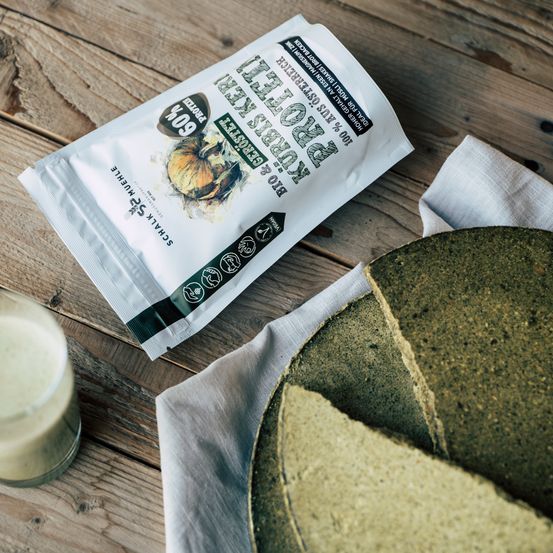 Ein Nahaufnahme eines grünen Smoothies auf einem Holztisch, neben einem Glas Getränk und einer Packung Spinatpulver.