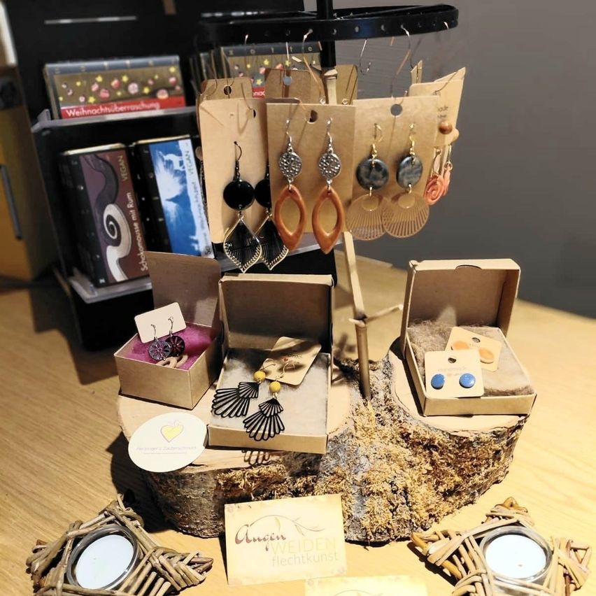 Eine Ausstellung verschiedener Ohrringe auf einem Holzstamm mit einem dekorativen Ständer. Die Ohrringe sind in verschiedenen Stilen und Farben. Einige sind in offenen Pappkartons, und andere hängen von einem Metallständer ab.