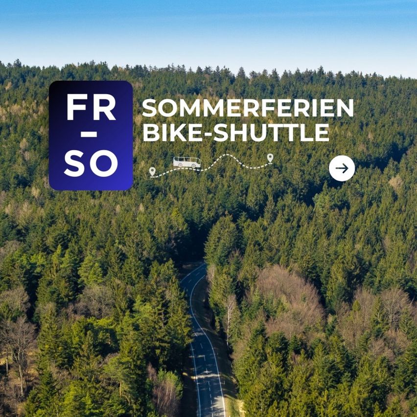 Luftaufnahme einer Waldstraße mit einem Bussymbol, das auf einen Fahrrad-Shuttle-Service für Sommerferien hinweist. Der Himmel ist klar und blau.