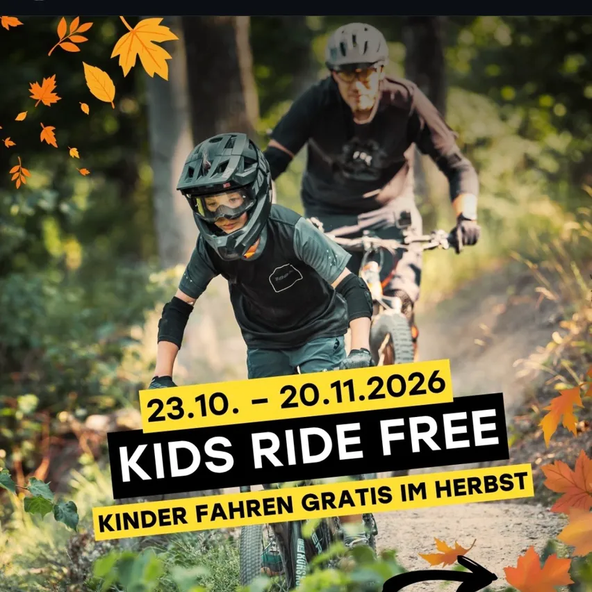 Zwei Personen fahren auf einem Waldweg mit Fahrrädern. Die Person vorne trägt einen Helm und eine Brille. Der Text auf dem Bild lautet 'Kinder fahren gratis' und die Daten '23.10. - 20.11.2026'.