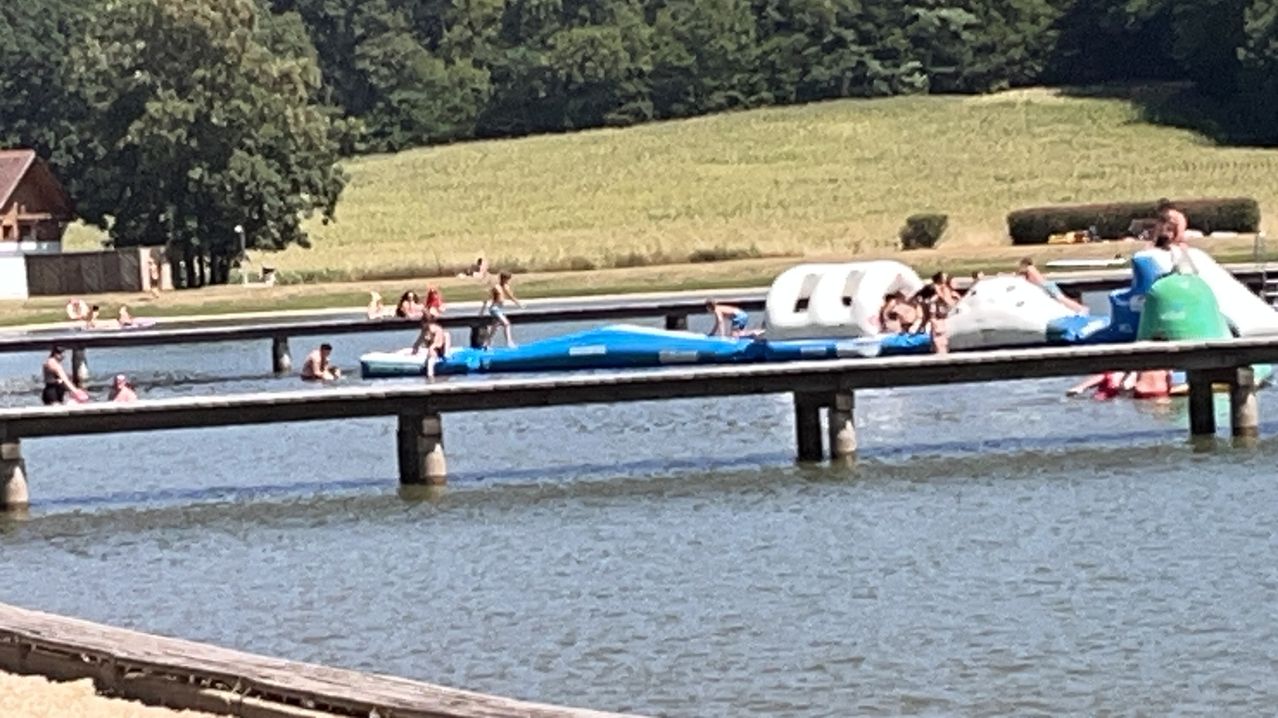 A group of people are enjoying a sunny day on a pier with inflatable water toys. Some are swimming in the water while others are on the pier.