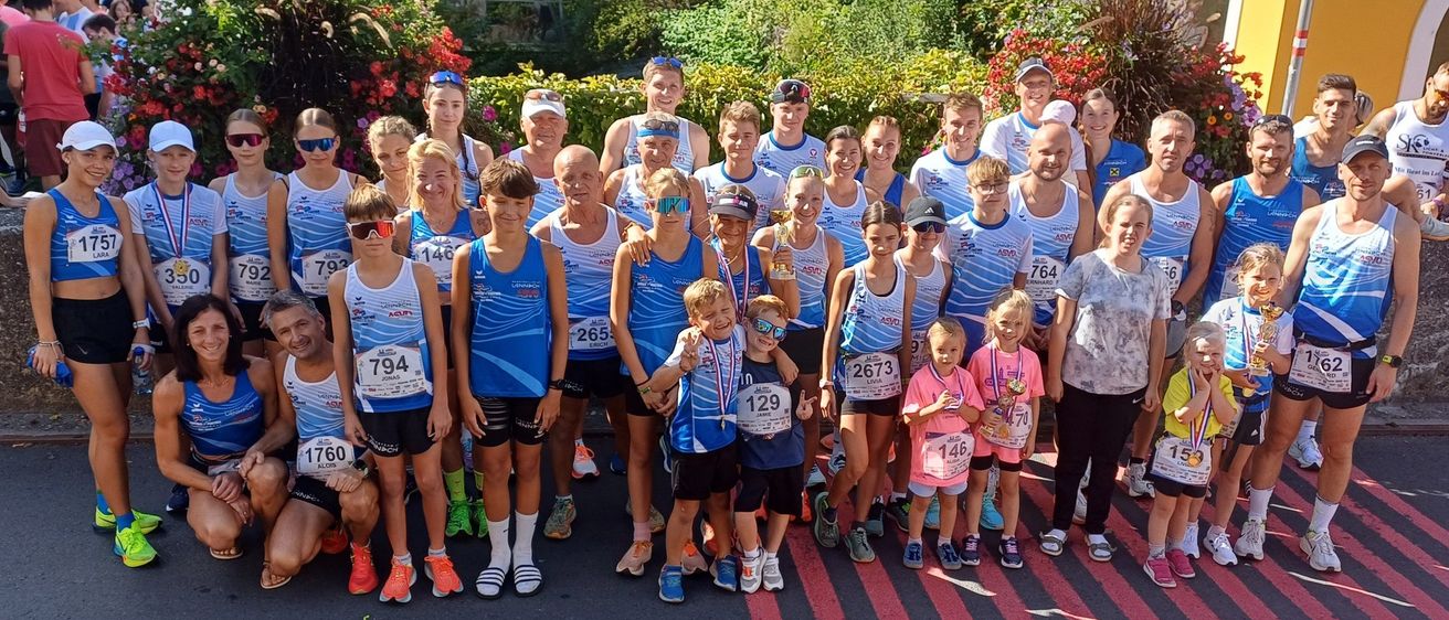 Eine Gruppe von Marathonläufern, einige mit Sonnenbrillen und Startnummern, posiert für ein Foto auf einer Straße. Sie sind von üppiger Grünfläche umgeben.