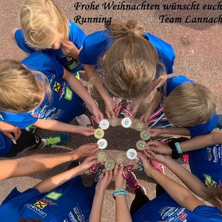 Gruppe von Kindern in blauen Trikots mit Medaillen versammelt sich im Kreis, mit einer festlichen Weihnachtsbotschaft von Team Lannach über ihnen.