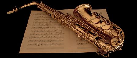 Ein goldenes Saxophon liegt auf einem Musikbogen. Das Saxophon hat eine glatte, polierte Oberfläche und komplizierte Designdetails. Der Musikbogen ist geöffnet, mit Noten und Symbolen in einem fließenden, komplexen Muster angeordnet.