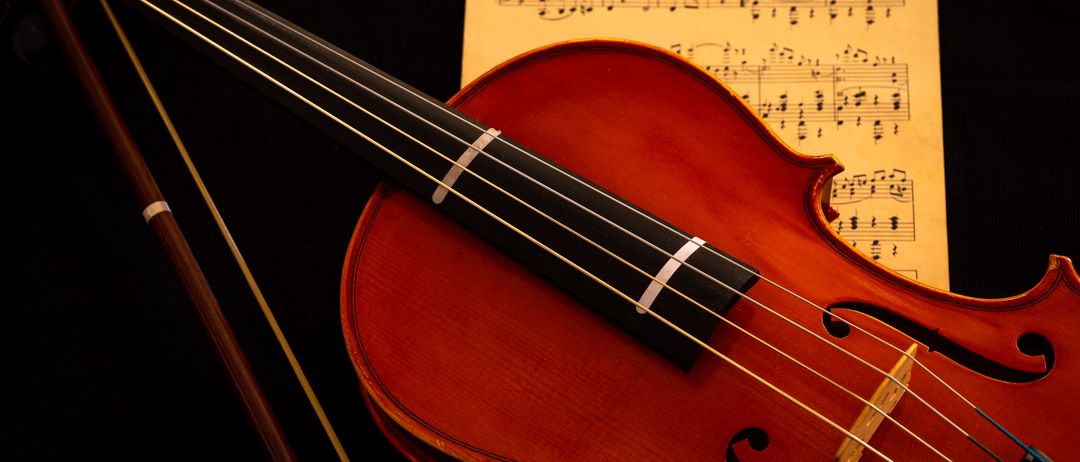 Eine rote Geige mit ihrem Bogen liegt auf einem Notenblatt mit Musiknoten. Der Korpus und der Bogen der Geige sind sichtbar, und die Noten auf dem Notenblatt sind lesbar.