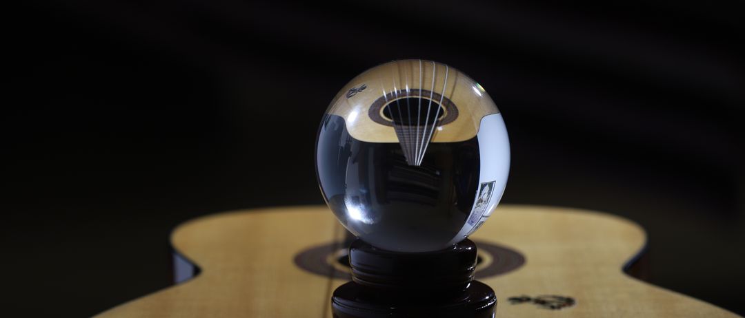 Ein Kristall-Papiergewicht liegt auf einer Gitarre. Die Gitarre hat einen schwarzen Hintergrund und steht auf einem Tisch.