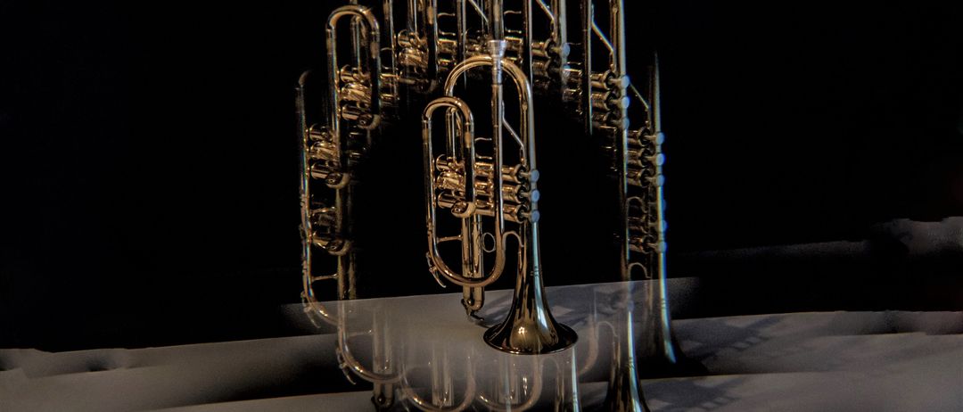 Eine Sammlung von Trompeten, die in einer Bogenform mit ihren Reflexionen auf einer weißen Oberfläche unter einem dunklen Hintergrund angeordnet sind.