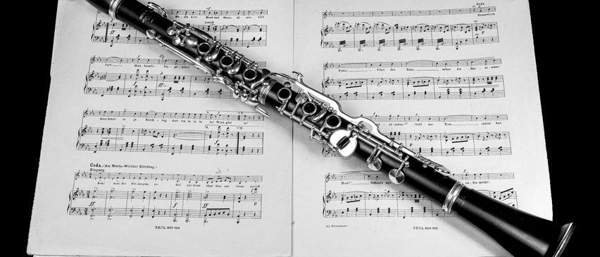 Eine schwarze und silberne Klarinette liegt auf einem Musikblatt. Das Musikblatt hat Noten und Symbole darauf geschrieben.