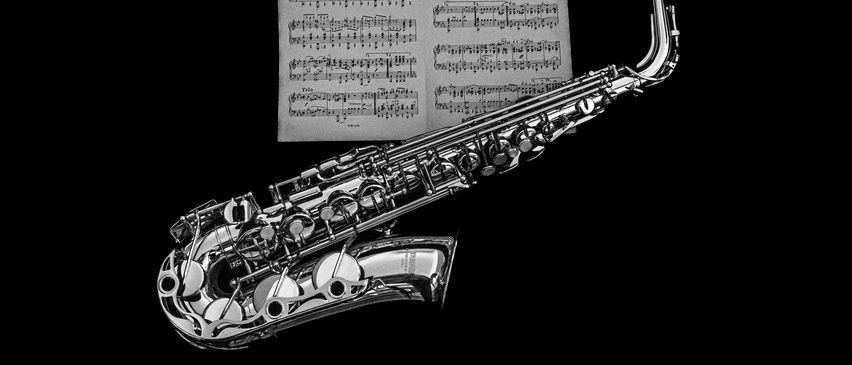 Ein silbernes Saxophon mit seinen Tasten und Mundstück lehnt sich an einen Hintergrund mit Musiknoten. Das Blatt enthält Musiknoten und Symbole, die möglicherweise ein Klavierstück angeben.