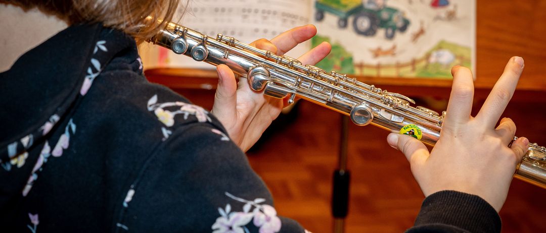 Eine Frau spielt Flöte und liest dabei Noten vor sich, trägt ein Blumenhemd.