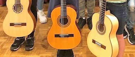 Eine Gruppe von Kindern und Jugendlichen posiert für ein Foto mit Gitarren in einem Raum mit roten Vorhängen.