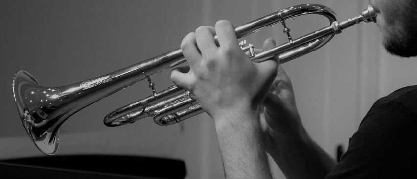 Ein Mann spielt eine Trompete drinnen, konzentriert auf seine Leistung mit einem Klavier dahinter.