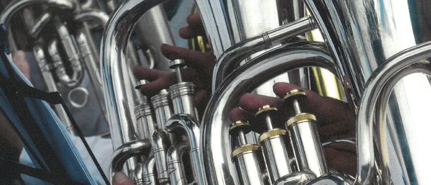 Eine Nahaufnahme von Blechblasinstrumenten, einschließlich Tubas und Trompeten, die von Händen gehalten werden. Die Instrumente haben eine glänzende, metallische Erscheinung.