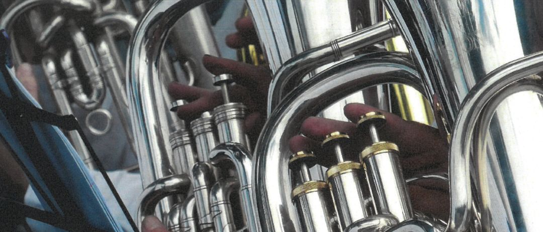 Eine Nahaufnahme von Blechblasinstrumenten, einschließlich Tubas und Trompeten, die von Händen gehalten werden. Die Instrumente haben eine glänzende, metallische Erscheinung.