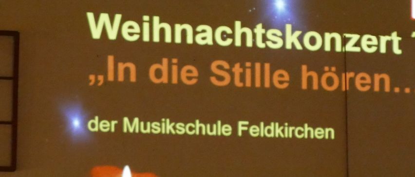 Eine Projektion zeigt 'Weihnachtskonzert 22, In die Stille horen...' mit einer Kerze und einem Handyverbotsschild.