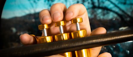 Eine Person spielt eine Trompete und hält sie mit beiden Händen. Die Trompete ist golden und hat eine glänzende Oberfläche. Die Person trägt einen Ring am Finger.