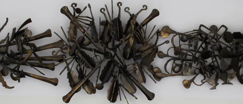 Eine Bronzeskulptur aus Musikinstrumenten, die in einem kreisförmigen Muster angeordnet sind. Verschiedene Instrumente wie Violinen, Trompeten und Celli sind kunstvoll verbunden. Eine Plakette am unteren Rand zeigt, dass sie von Wolfgang A. Hochinger stammt.