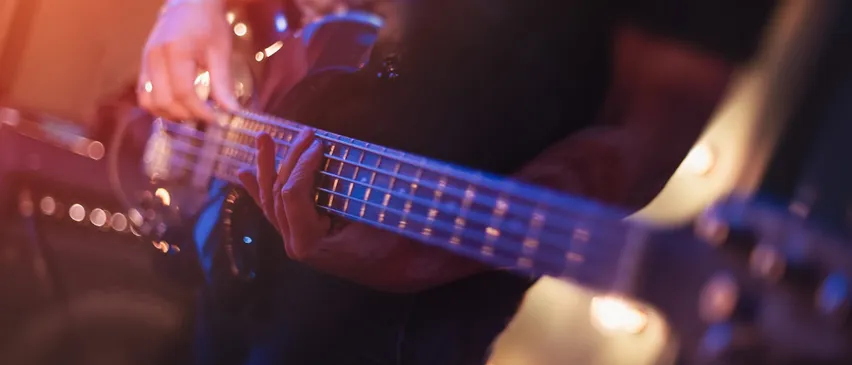 Ein Musiker spielt eine elektrische Bassgitarre auf der Bühne, wobei blaue Lichter die Szene beleuchten.