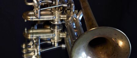 Ein Messing-Posaune mit Ventilen wird auf schwarzem Hintergrund ausgestellt. Das Instrument hat mehrere Ventile und eine große Glocke.