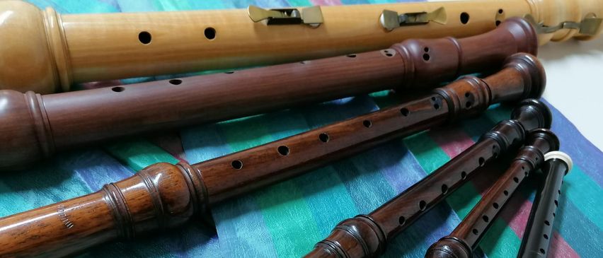 Mehrere hölzerne Blockflöten in verschiedenen Größen sind auf einem mehrfarbigen Tuch angeordnet. Die Blockflöten haben Metalltasten und sind ordentlich zusammengestellt.