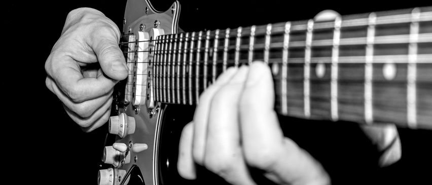 Schwarz-Weiß-Bild von Händen, die eine E-Gitarre spielen. Die Finger drücken auf die Saiten.