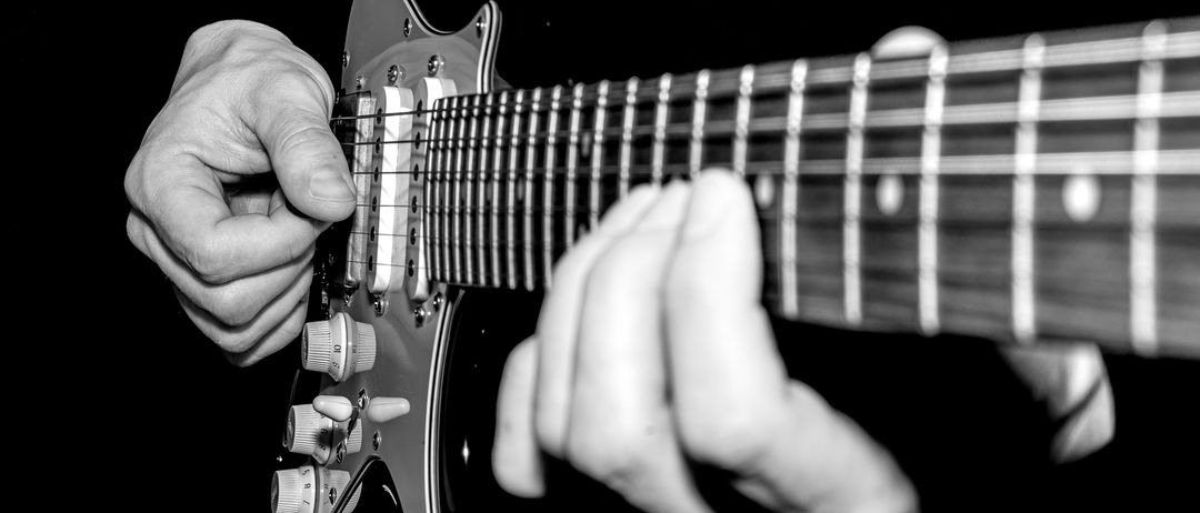 Schwarz-Weiß-Bild von Händen, die eine E-Gitarre spielen. Die Finger drücken auf die Saiten.
