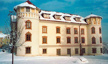 Ein großes weißes Gebäude mit vielen Fenstern und einem Turm, der von Schnee bedeckt ist. Das Gebäude ist von Schnee umgeben, und ein Baum steht davor.