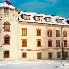 Ein großes weißes Gebäude mit vielen Fenstern und einem Turm, der von Schnee bedeckt ist. Das Gebäude ist von Schnee umgeben, und ein Baum steht davor.