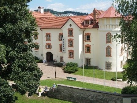 Ein Blick von oben auf ein großes weißes Gebäude mit rotem Dach, umgeben von Bäumen und Rasen.