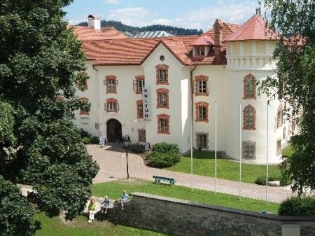 Ein Blick von oben auf ein großes weißes Gebäude mit rotem Dach, umgeben von Bäumen und Rasen.