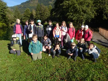 Eine Gruppe von Kindern steht in einem Grasbereich mit Bäumen und Bergen im Hintergrund. Sie lächeln und scheinen für ein Foto zu posieren.
