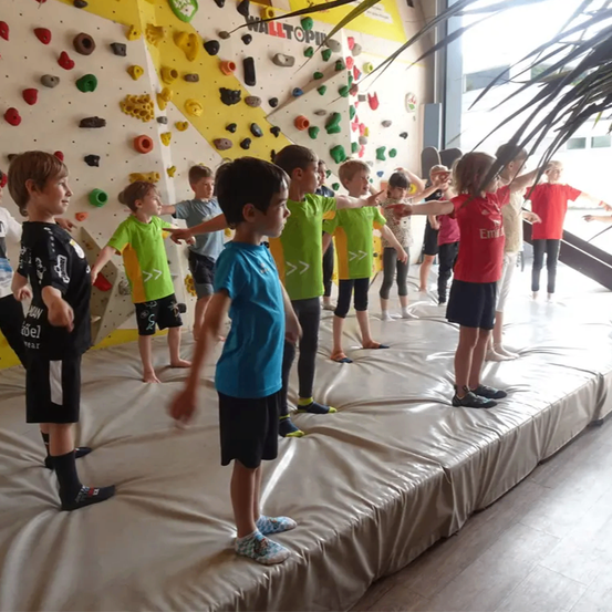 Mehrere Kinder stehen auf einer Bühne mit Kletterwänden im Hintergrund und üben für eine Aufführung.