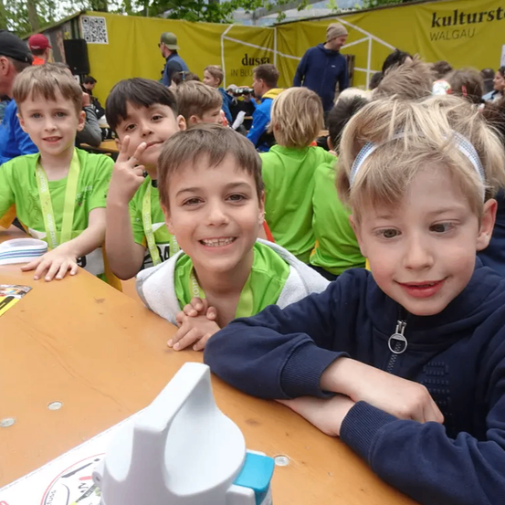 Eine Gruppe junger Jungen, die grüne T-Shirts tragen, sitzen lächelnd an einem Tisch, mit einem gelben Banner im Hintergrund.