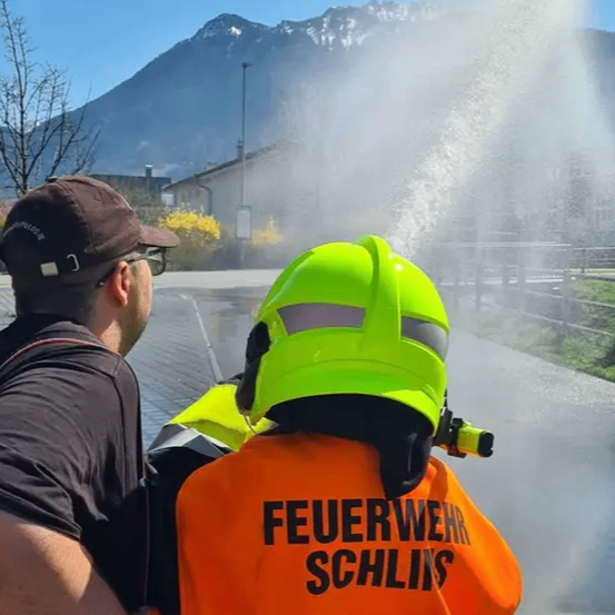 Ein Feuerwehrmann sprüht Wasser aus einem Hydranten in einer Stadt mit Bergen im Hintergrund.