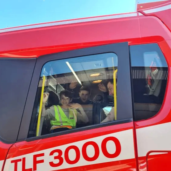 Ein rotes Fahrzeug mit der Nummer 3000. Im Inneren winkt ein Junge in einer Sicherheitsweste aus dem Fenster.