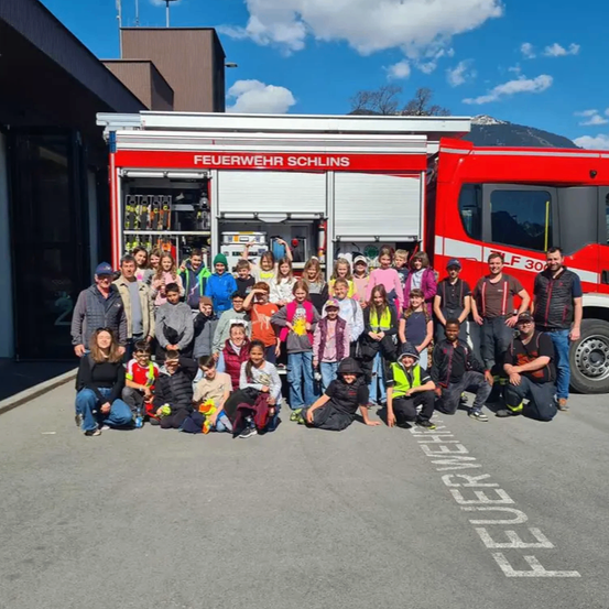 Eine Gruppe von Kindern und Erwachsenen posiert für ein Foto vor einem roten Feuerwehrauto mit der Aufschrift 'Feuerwehr Schänis'.