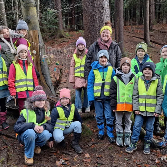 Eine Gruppe von Kindern und Erwachsenen in Warnwesten posiert für ein Foto im Wald. Die Erwachsenen stehen hinter den Kindern, und alle lächeln.