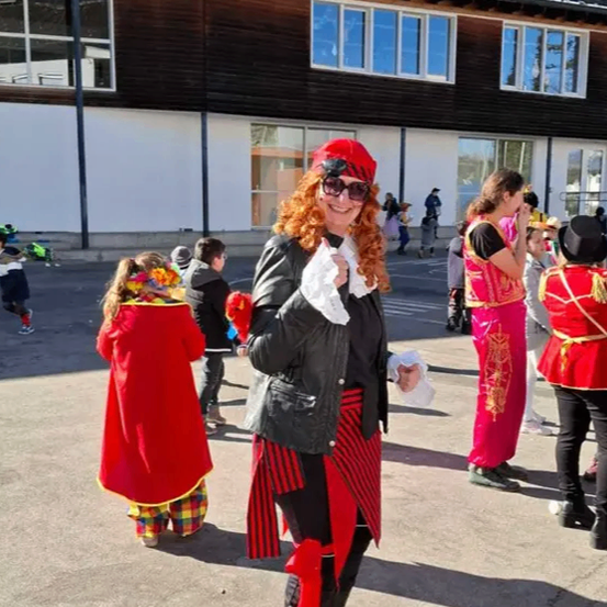 Eine Frau in einem roten und schwarzen Kostüm mit einem roten Hut steht draußen auf einem Parkplatz mit Kindern und Erwachsenen.