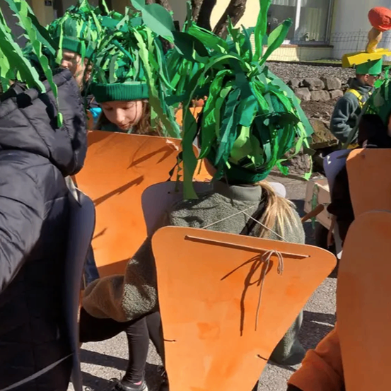 Eine Gruppe von Menschen in Karottenkostümen, jeder mit einer grünen Laubheaddress, geht auf einer Straße.