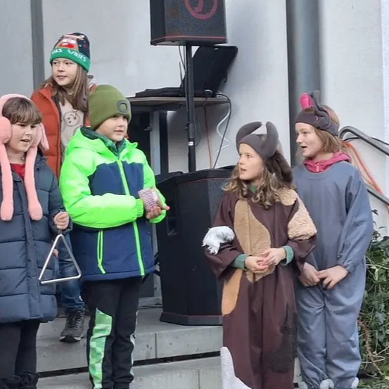 Fünf Kinder in verschiedenen Kostümen stehen auf einer Betontreppe. Ein Kind hält ein Dreieck und ein anderes trägt einen Hut mit einem rosa Ohr.